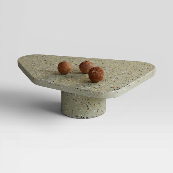 Mesa de centro MEZAS Passeio em granilite verde com base cilíndrica e tampo assimétrico. Três cocos decoram a superfície.